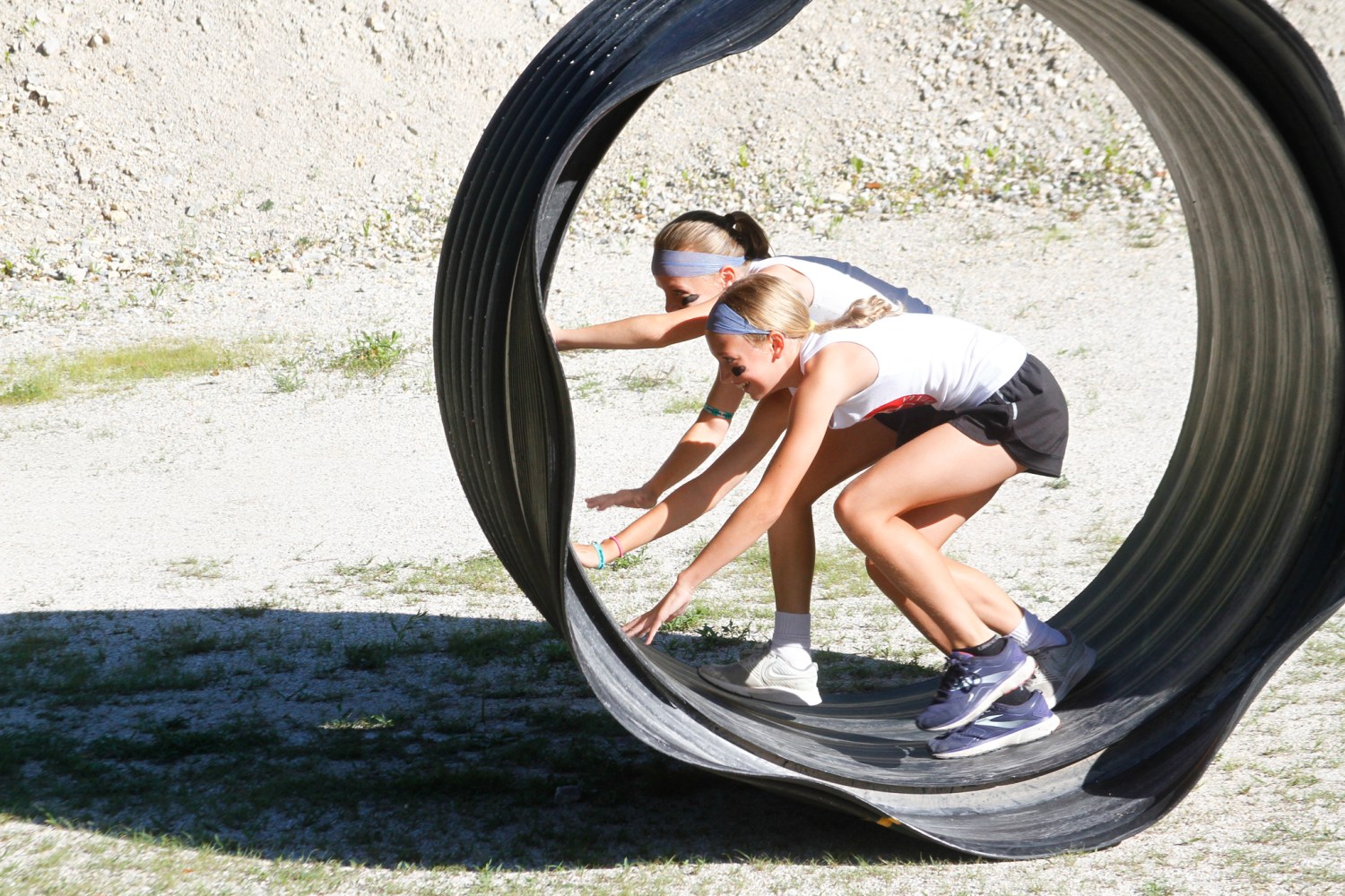 Two girls balancing inside a large rolling tire outdoors.