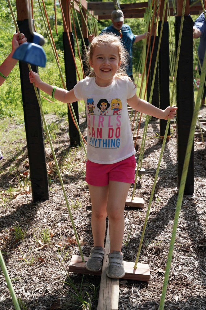 Smiling child on a rope bridge in a park.